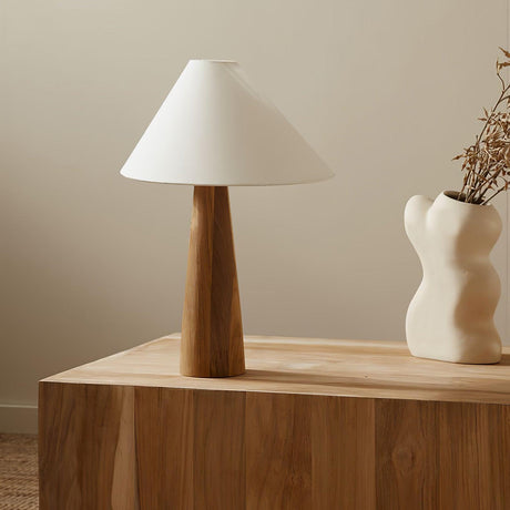 Wood cone lamp unlit on a wood block in a corner beside a vase