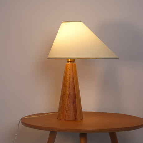 Wood cone lamp lit warm on a round wood table against a pink wall