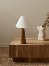 Wood cone lamp unlit on a solid wood block beside a white vase