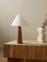 Wood cone lamp unlit on a wood block beside a curved white vase