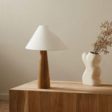 Wood cone lamp unlit beside dried branches in a white vase