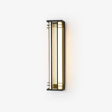 Black box outdoor wall light with gold tone trim and a ribbed acrylic panel, lit warm