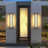 A pair of box lights lit on either side of a tall lit window in a white facade
