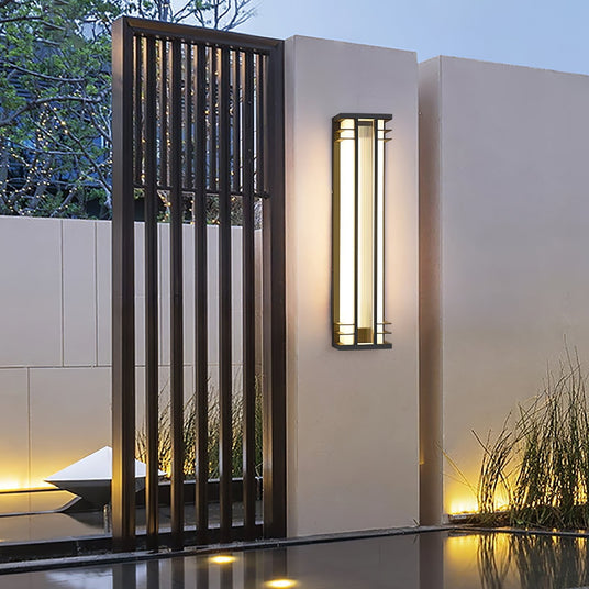 A box light lit on a white wall beside a slatted black screen panel and a pool
