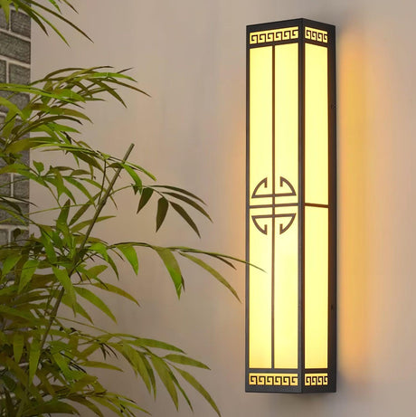 The lantern lit on a pale wall behind the leaves of a bamboo plant