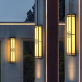 Three tall lanterns lit on facade walls beside a glass doorway at dusk
