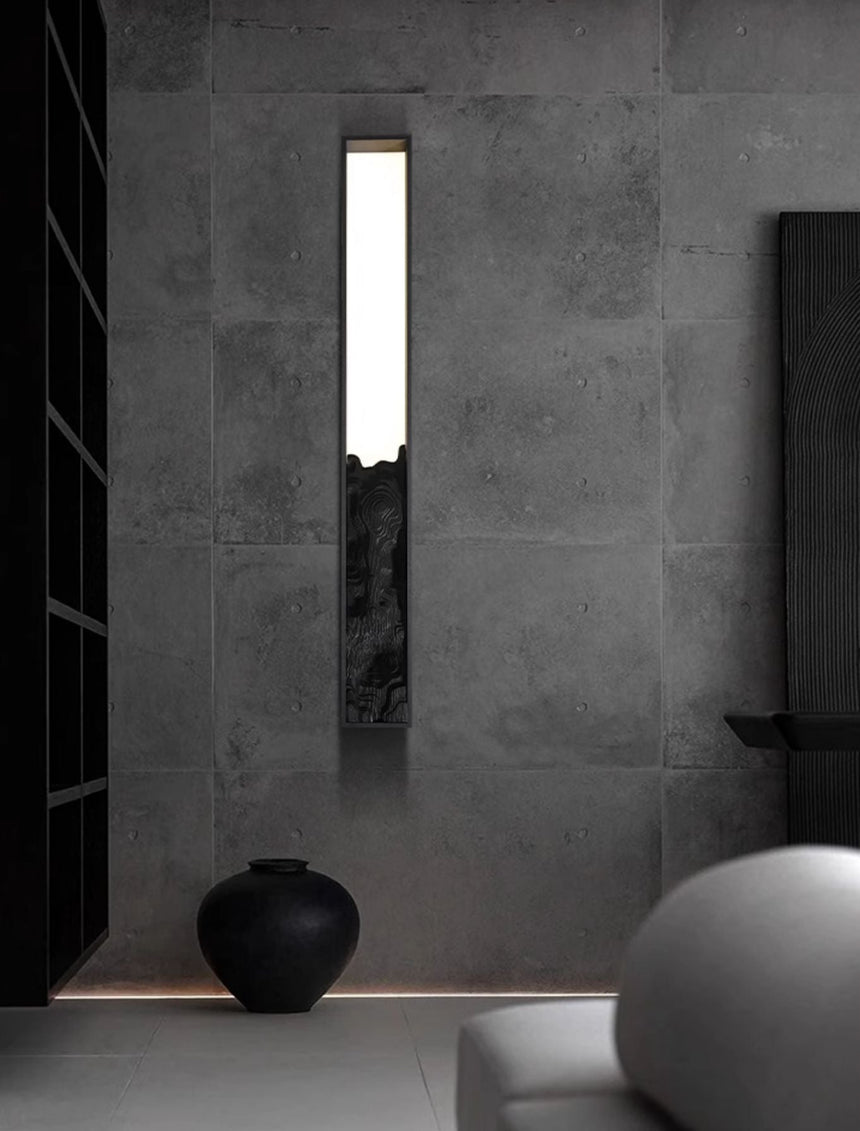 Bar upright on a concrete wall beside a dark vase and a round sculpture