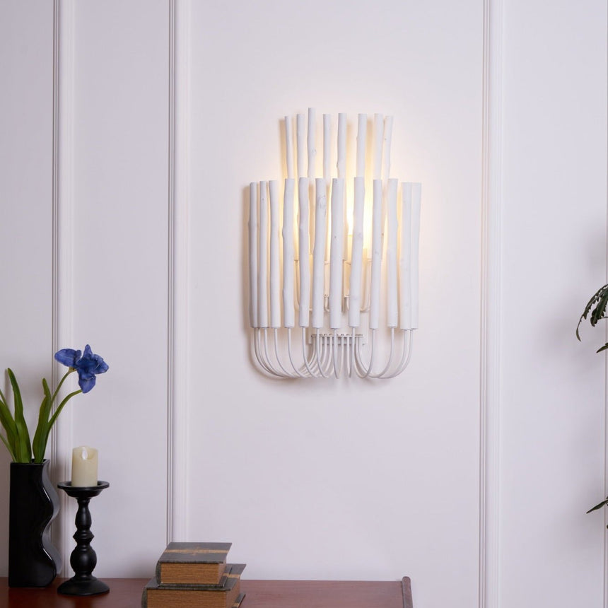 Rod sconce lit on a paneled wall above a table with books and candles