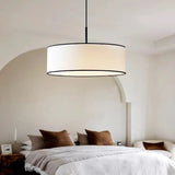 Fabric drum pendant light above a bed with a linen throw