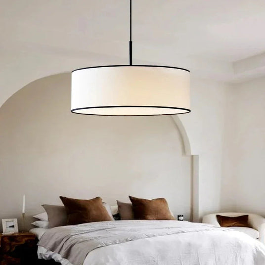 Fabric drum pendant light above a bed with a linen throw