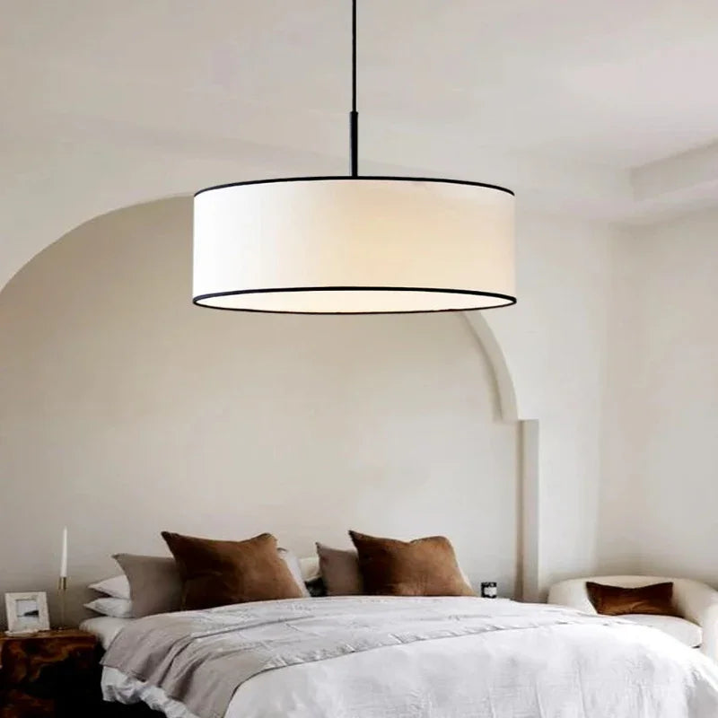 Fabric drum pendant light above a bed with a linen throw