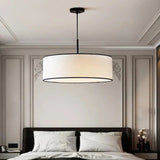 Fabric drum pendant light in a paneled bedroom seen from the foot of the bed