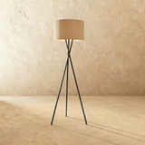 A beige fabric drum shade on a slim black tripod of three crossed metal legs