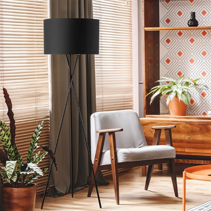 The lit lamp beside a window blind and a pale armchair in a patterned room