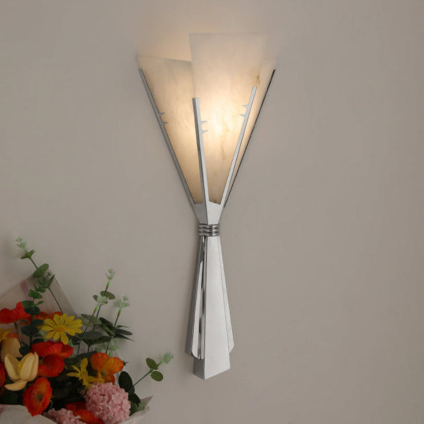 The large fan sconce lit on a taupe wall above a bouquet of flowers