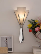The fan sconce lit above a shelf with a framed print and colorful flowers