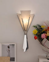 The fan sconce lit above a table with a framed photo and a bouquet of flowers