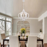 The crown lit in a pale dining room above a table and upholstered chairs