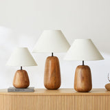 Farmhouse table lamp lit on a wooden nightstand beside a bed and books