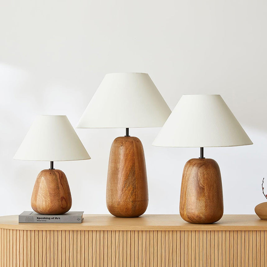 Farmhouse table lamp lit on a wooden nightstand beside a bed and books