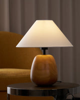 Farmhouse table lamp lit on a dark table in front of a yellow chair