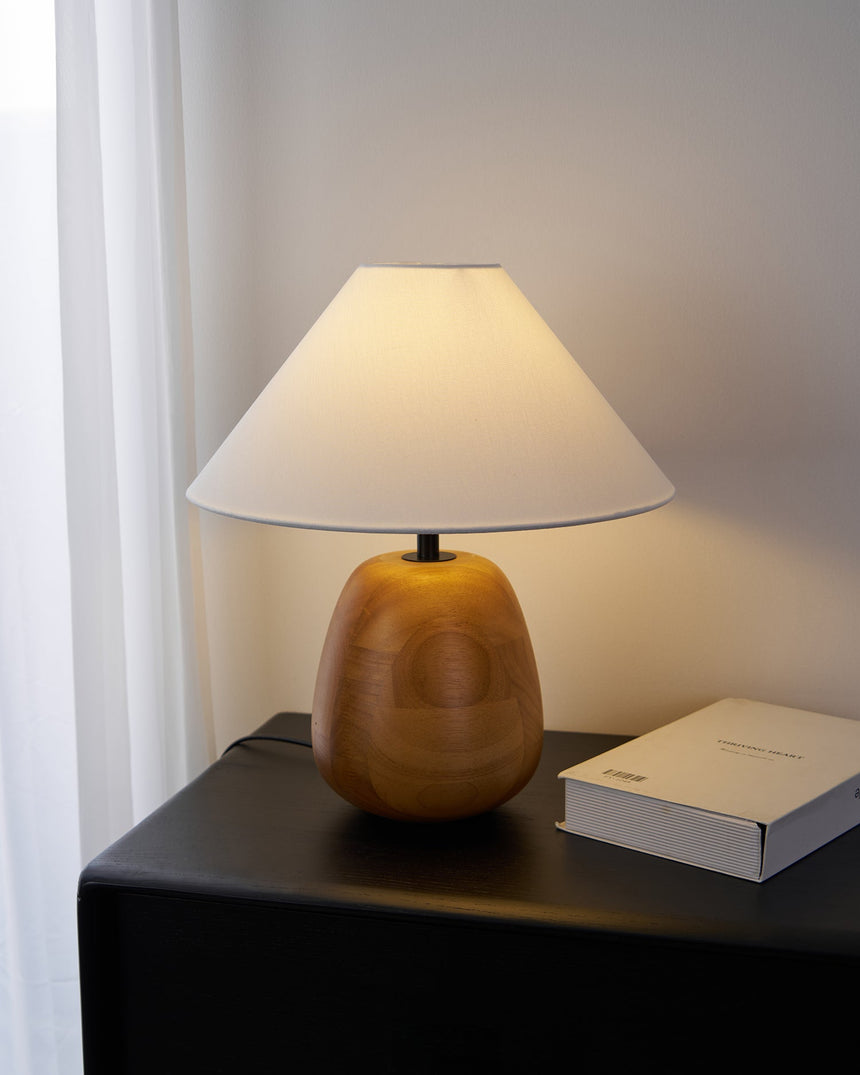 Farmhouse table lamp lit on a black nightstand beside an open book