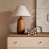 Farmhouse table lamp on a wooden cabinet in front of a textured wall piece