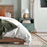 Farmhouse table lamp lit on a green nightstand beside a made bed