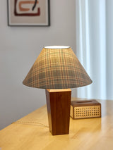 Plaid shade lamp lit on a pale desk beside a small woven box