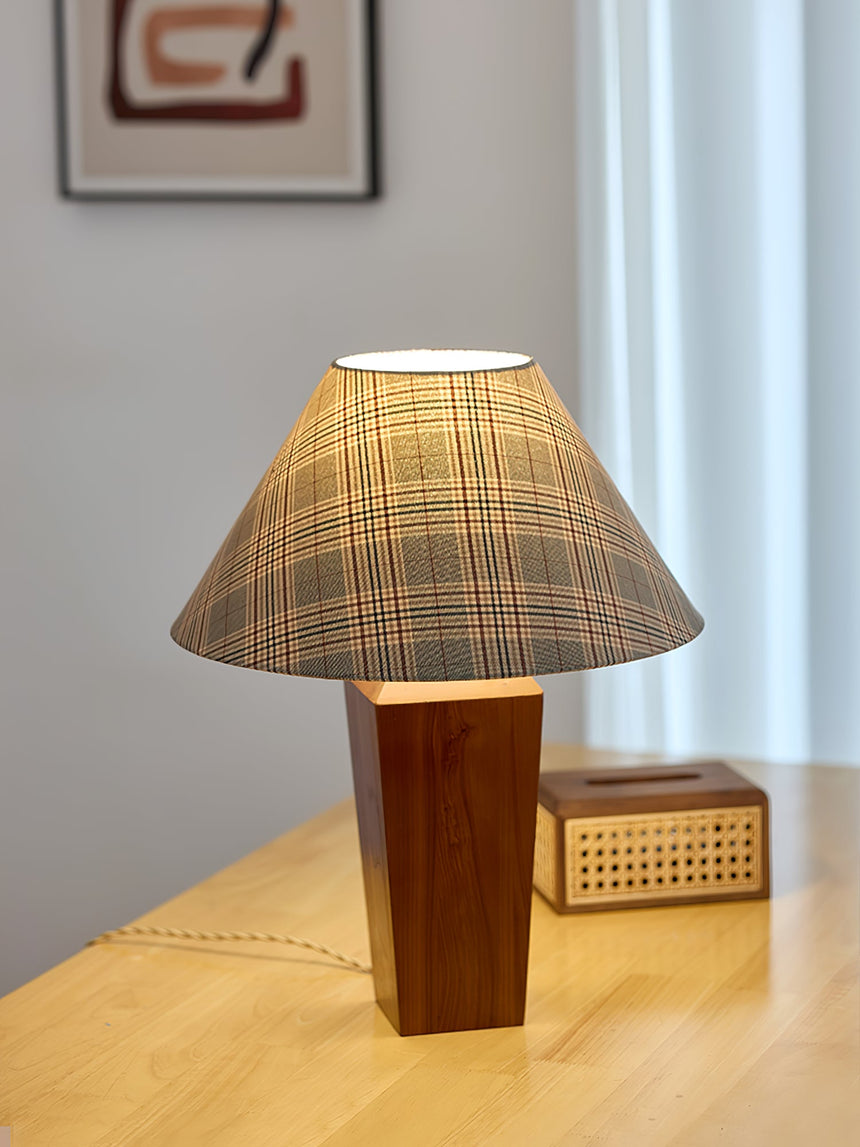 Plaid shade lamp lit on a pale desk beside a small woven box