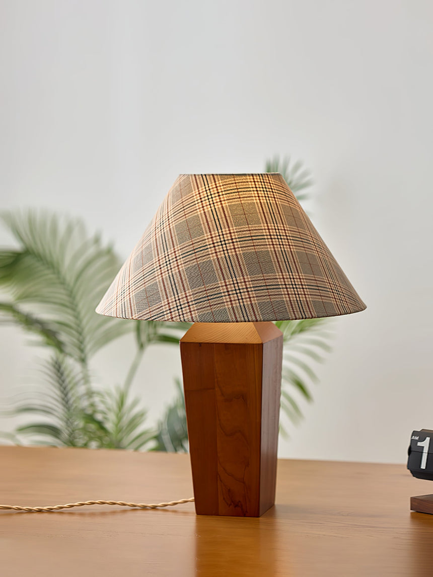 Plaid shade lamp lit on a wood desk beside a green plant