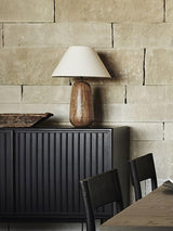 Farmhouse table lamp lit on a dark console in front of a stone wall