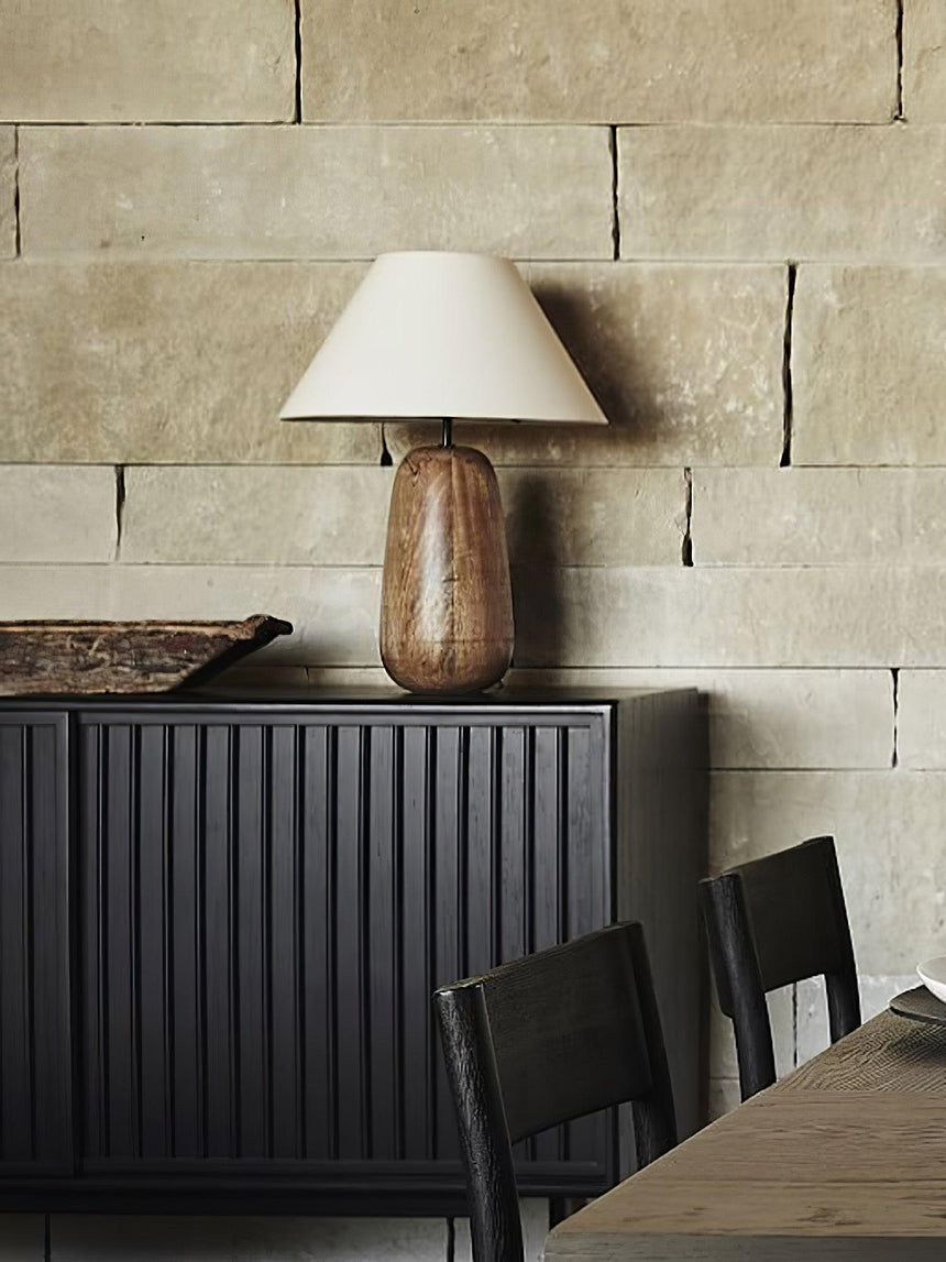 Farmhouse table lamp lit on a dark console in front of a stone wall
