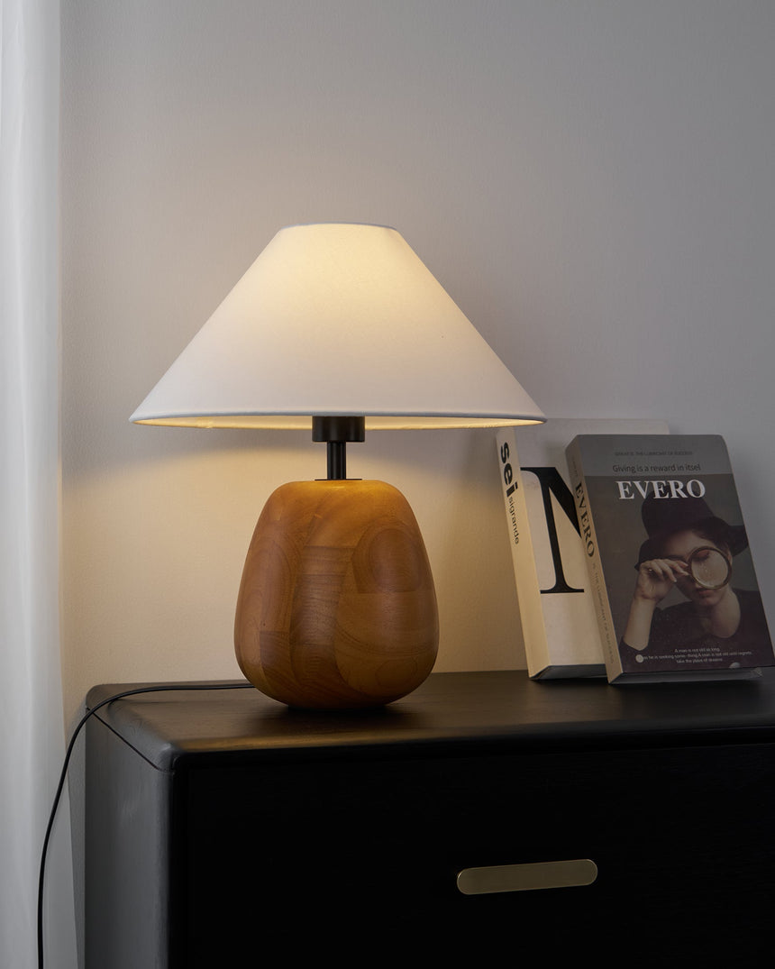 Farmhouse table lamp lit on a dark chest beside stacked magazines