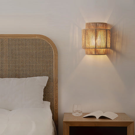 The hemp lamp lit above a cane headboard and a wood nightstand with a book