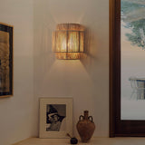 The hemp lamp lit on a white wall above a framed photo and a clay vase