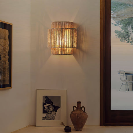 The hemp lamp lit on a white wall above a framed photo and a clay vase