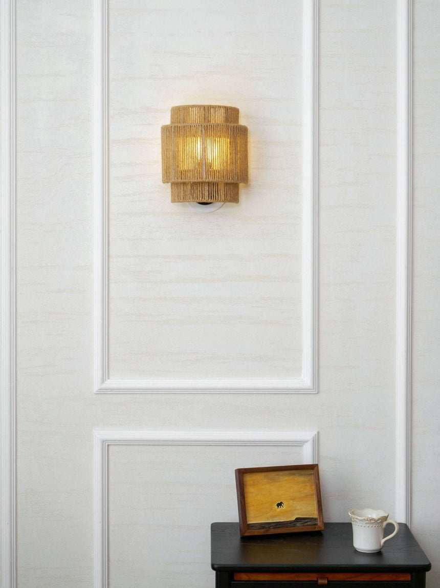 The hemp lamp on a white paneled wall above a small dark nightstand