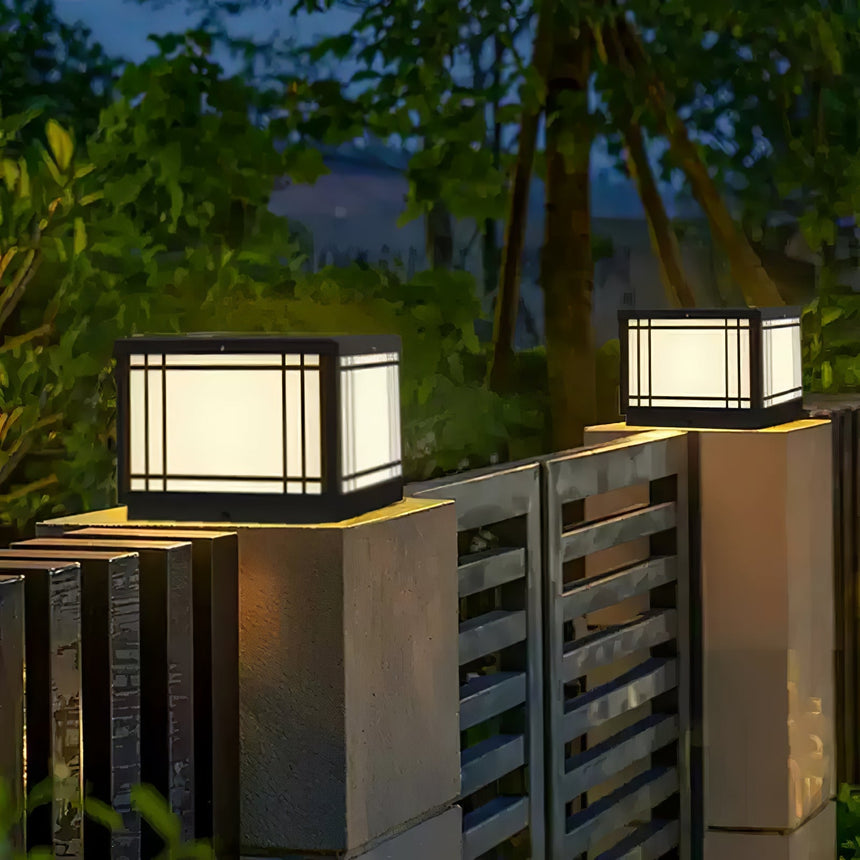 Lit lanterns on two pillars with trees and an evening sky behind
