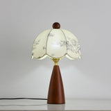 Floral table lamp lit and seen at an angle against a pale ground