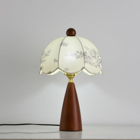 Floral table lamp lit and seen at an angle against a pale ground