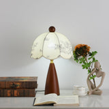 Floral table lamp lit beside a pale stone figurine and books