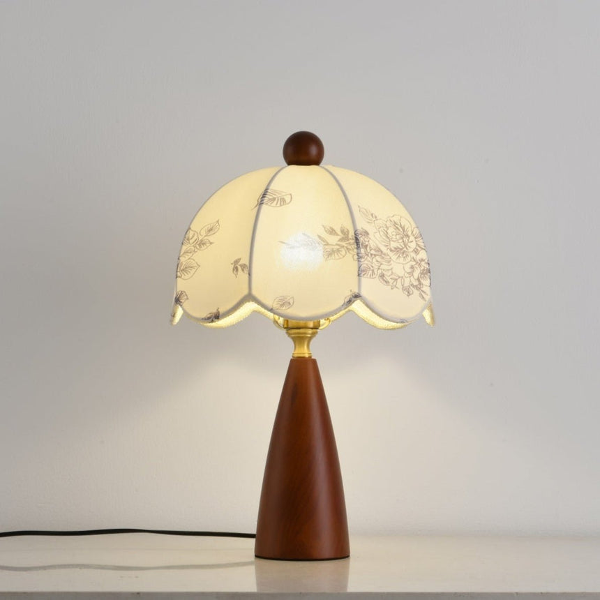 Floral table lamp lit and seen from the front on a pale ground