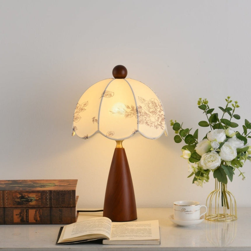Floral table lamp lit beside white roses and a stack of old books