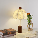 Parasol shade lamp lit on a desk beside an open book and a cup
