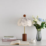 Parasol shade lamp unlit on a desk beside white and blue roses