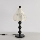 Black floral table lamp unlit against a pale wall, petal shade closed