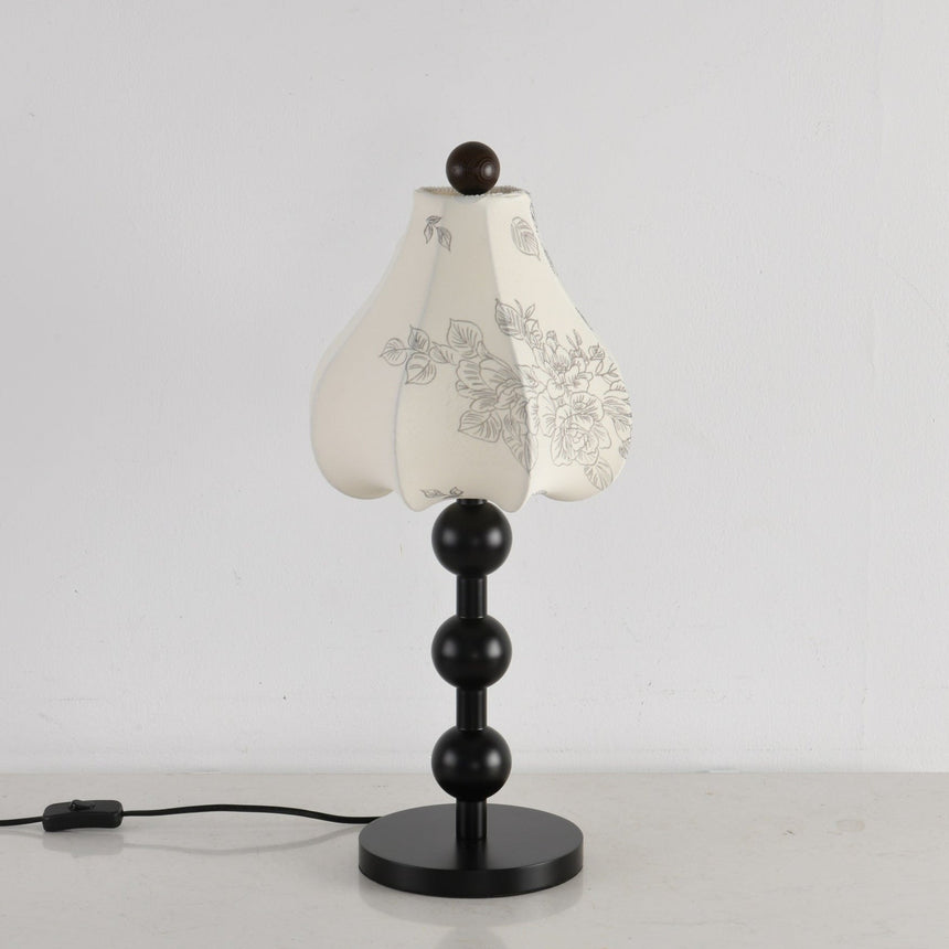 Black floral table lamp unlit against a pale wall, petal shade closed