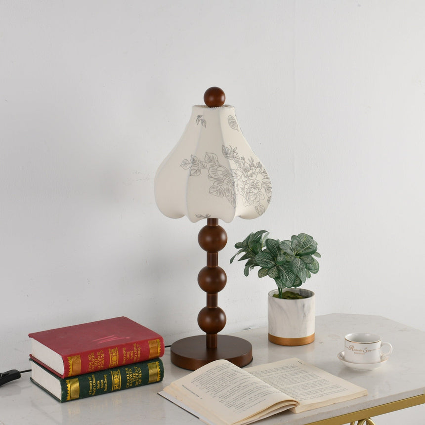Black floral table lamp on a table beside red bound books and a cup