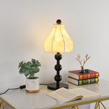 Floral table lamp lit on a console beside a plant and an open book